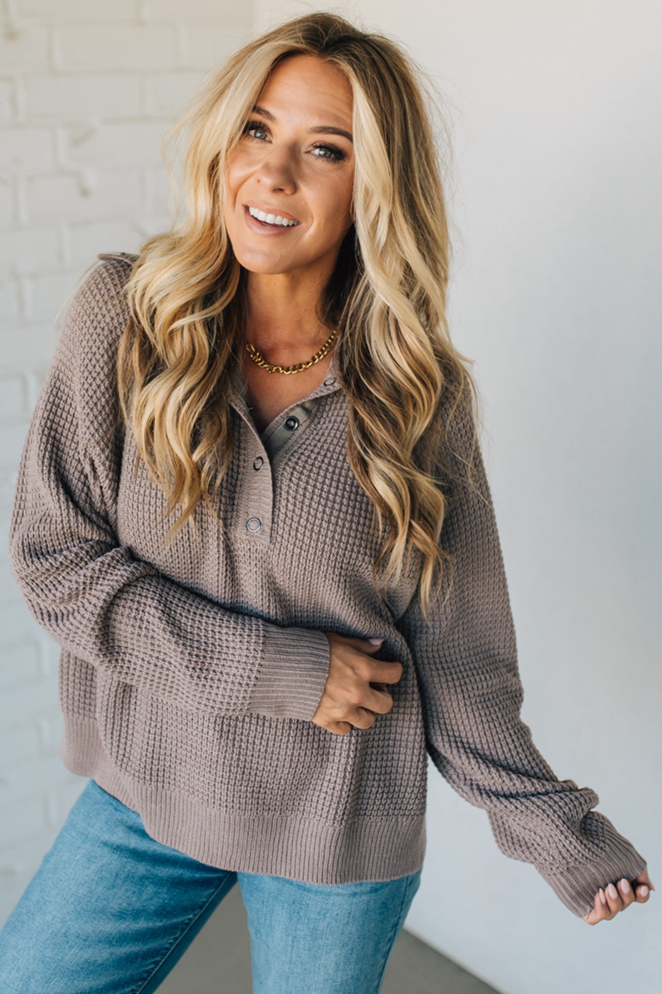 Woman wearing a brown sweater and blue jeans against a white background