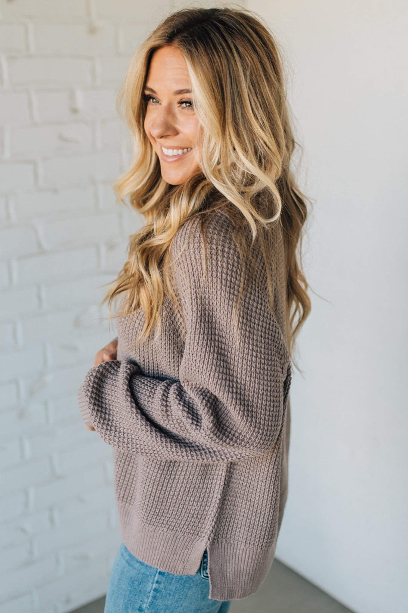 Woman wearing a brown knitted sweater against a white brick wall
