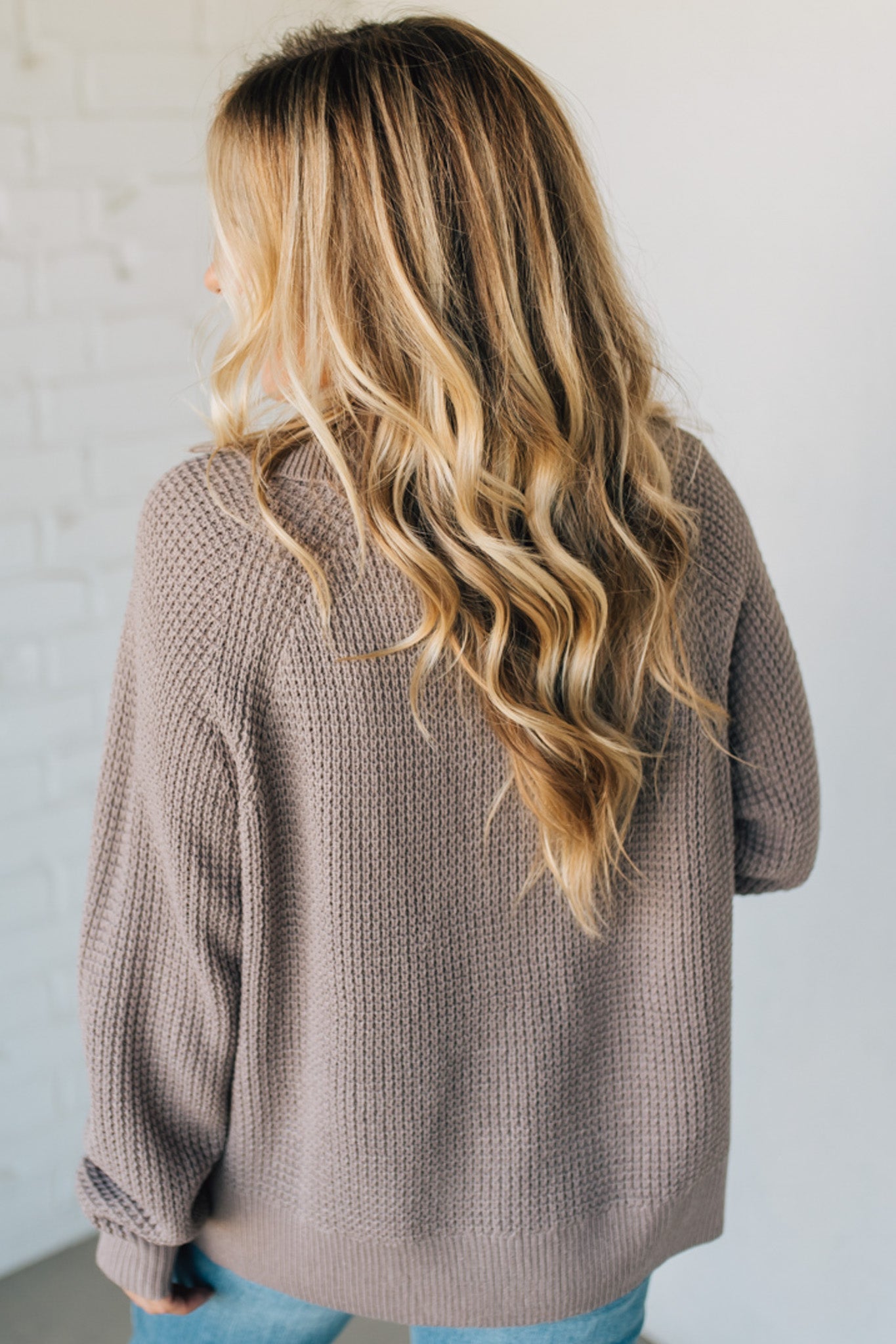 Person wearing a brown knitted sweater with a plain background