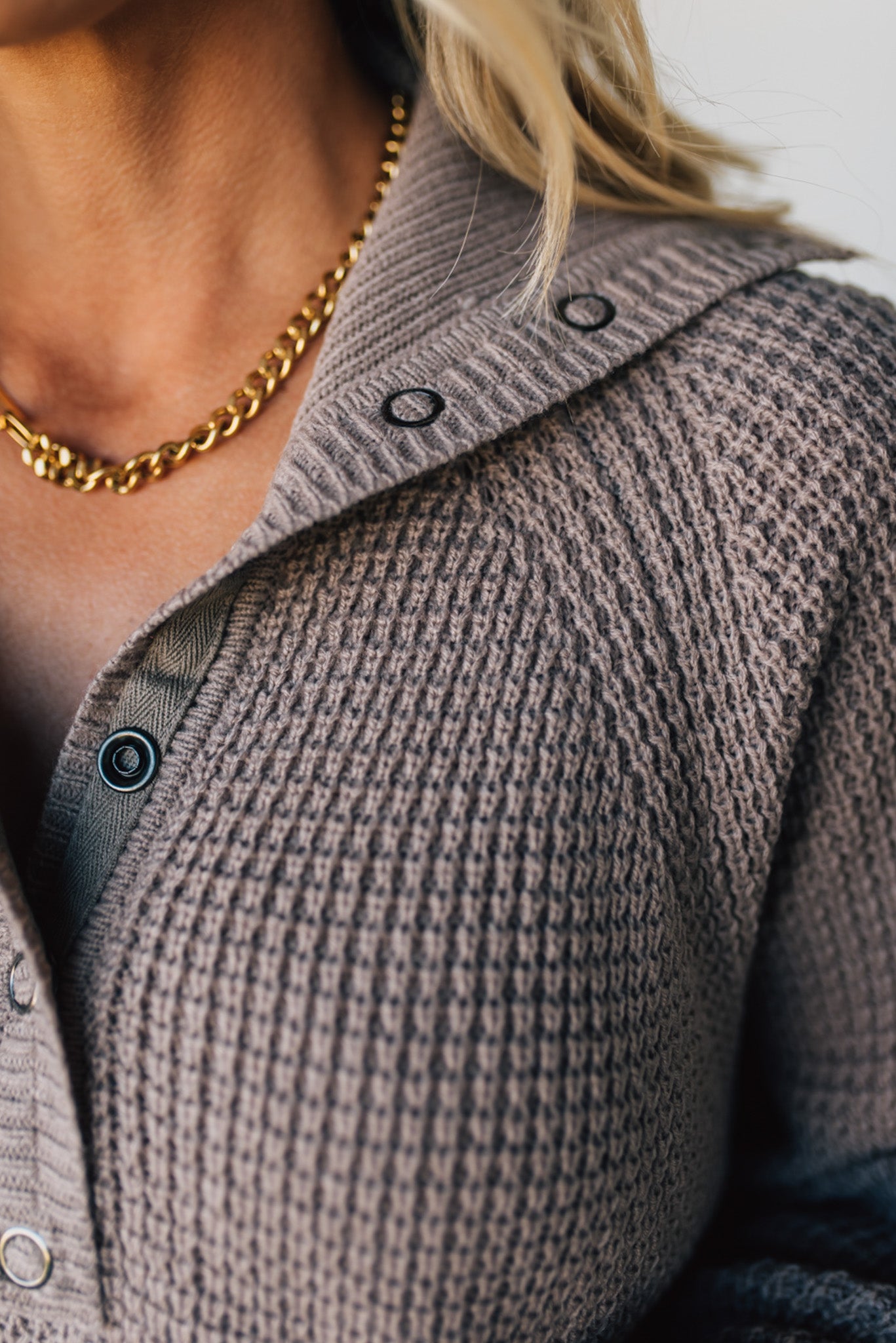 Close-up of a person wearing a textured brown cardigan with a gold chain necklace.