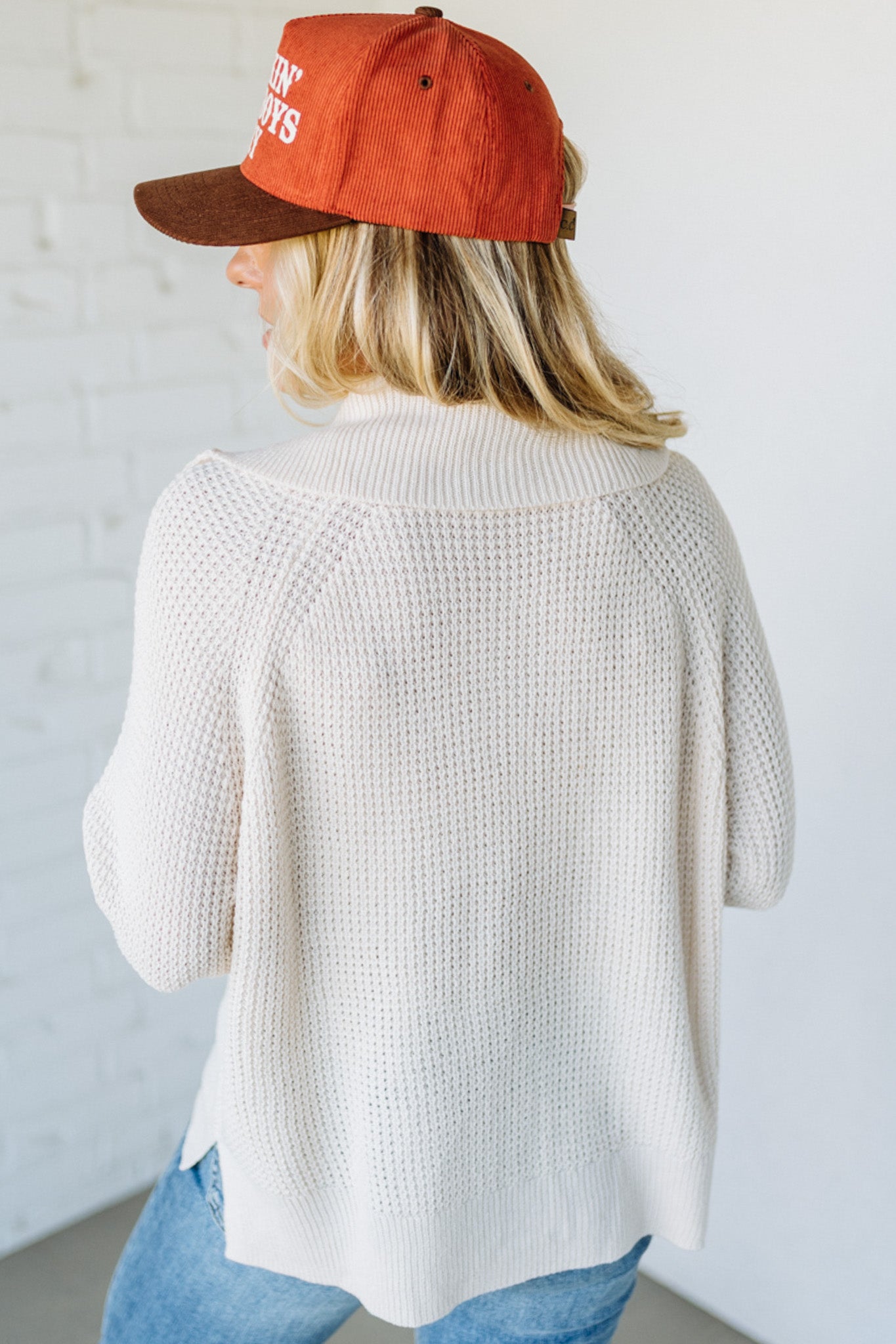 Person wearing a red cap and white cardigan with a blurred background