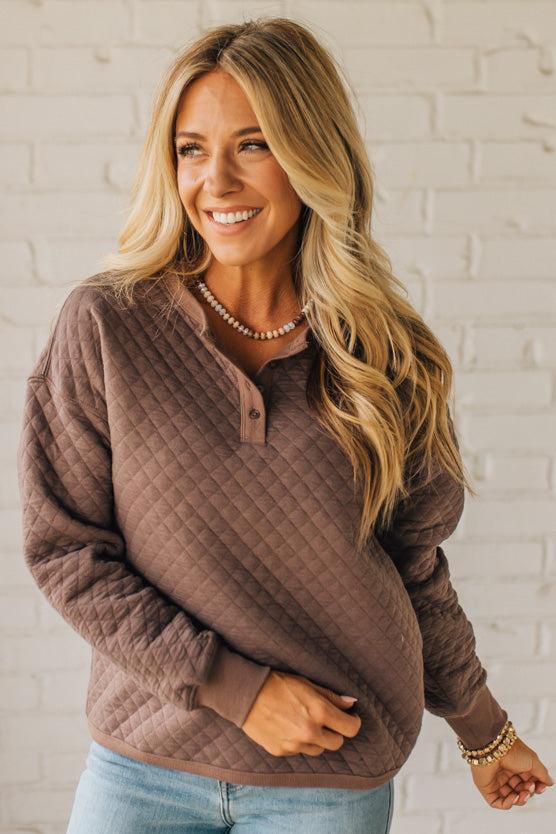 Woman wearing a brown quilted sweater against a white brick wall