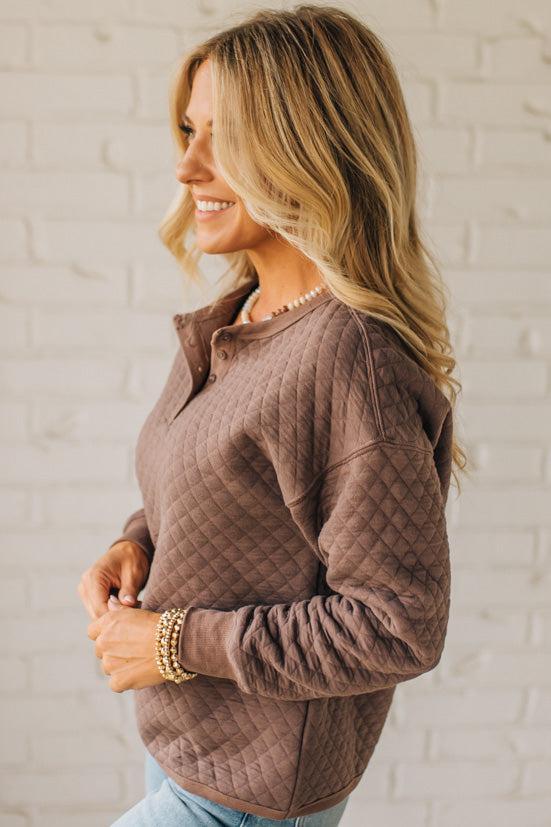 Woman wearing a brown quilted jacket against a white brick wall