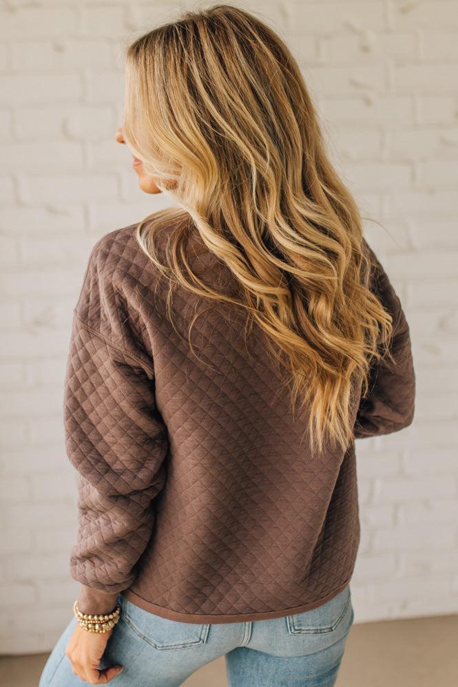 Person wearing a brown quilted jacket with a neutral background