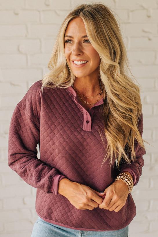 Woman wearing a quilted purple pullover against a white brick wall