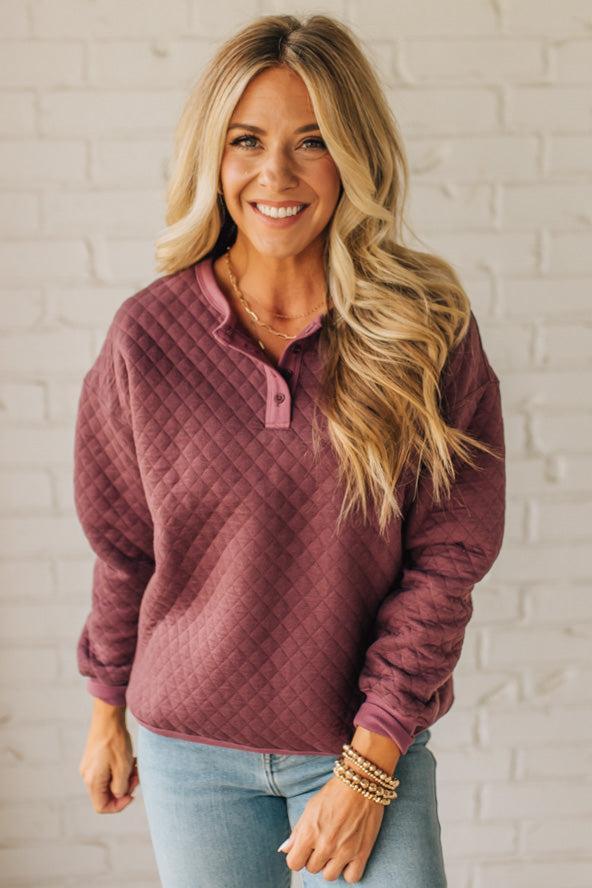 Woman wearing a maroon quilted pullover against a white brick wall