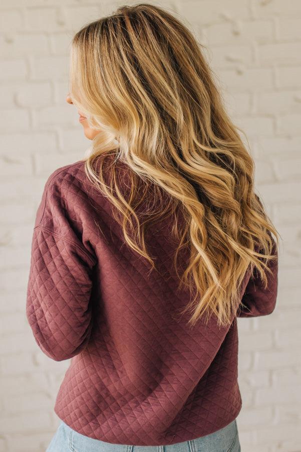 Woman wearing a maroon quilted jacket against a white brick wall