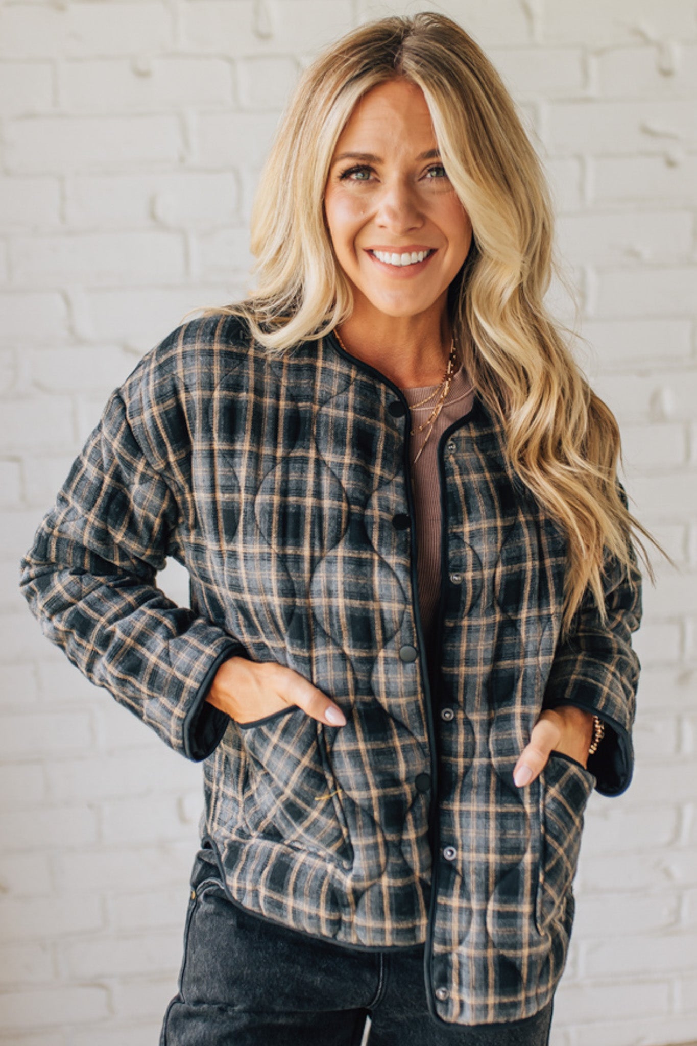 Woman wearing a plaid jacket in front of a white brick wall