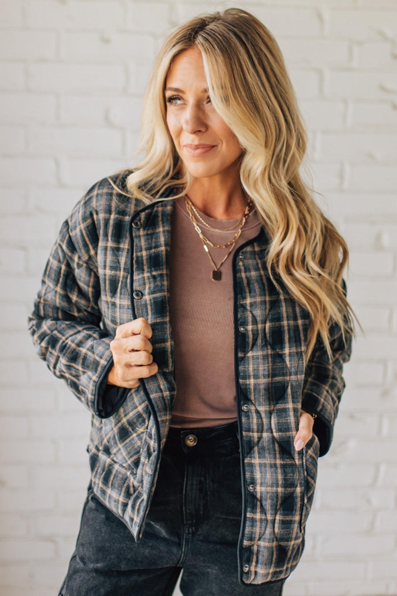 Woman wearing a plaid shirt over a brown top with a white brick wall background