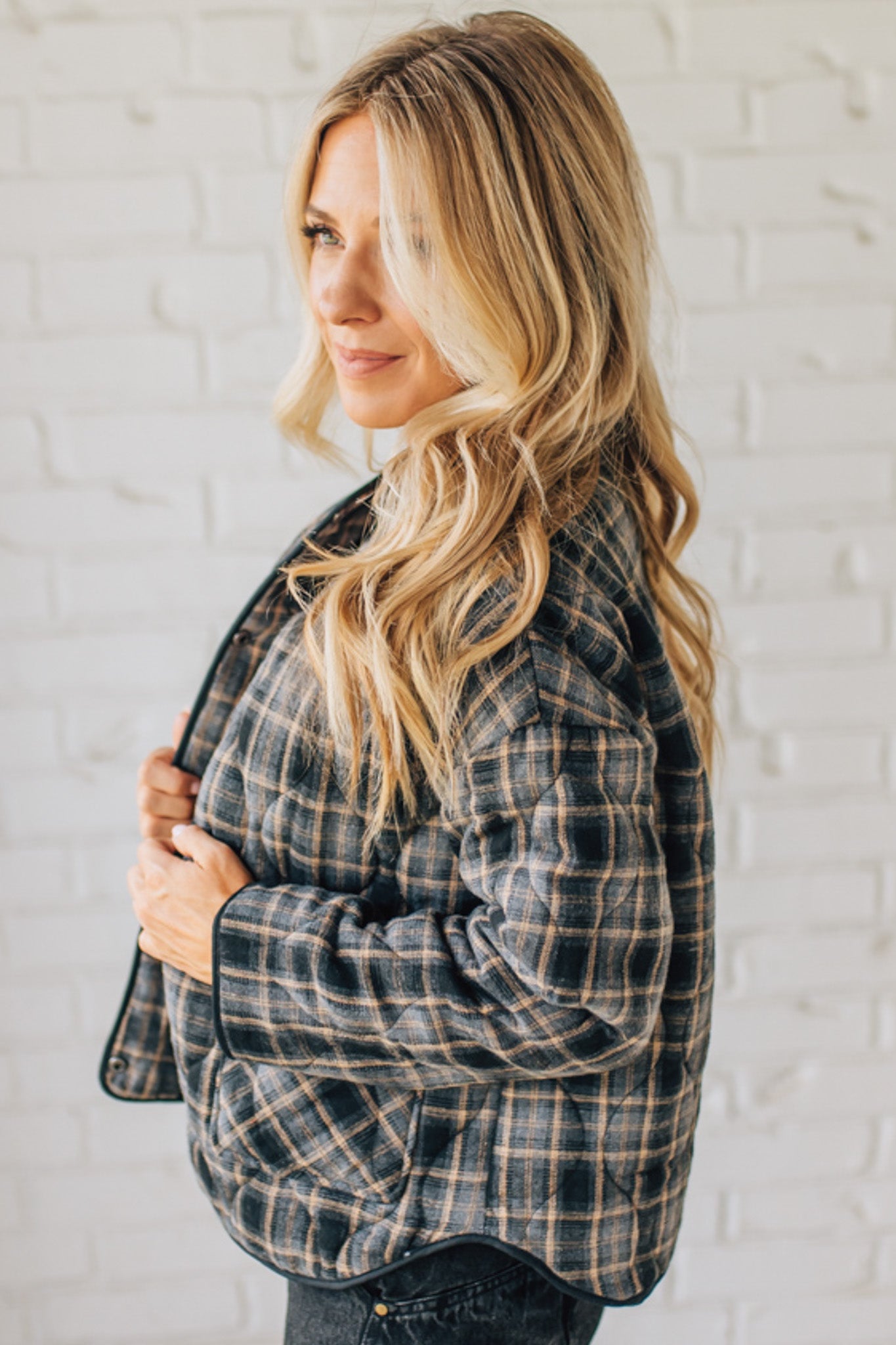 Woman wearing a plaid jacket against a white brick wall