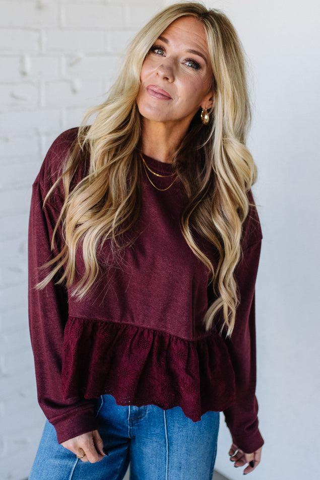 Blonde woman wearing a wine colors sweatshirt with peplem hem in eyelet lace.