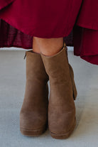 Person wearing brown ankle boots with block heel and smooth faux suede finish.