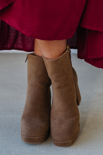 Person wearing brown ankle boots with block heel and smooth faux suede finish.