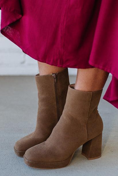 Person wearing brown ankle boots with block heel and smooth faux suede finish.