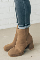 Person wearing brown ankle boots with block heel and smooth faux suede finish.