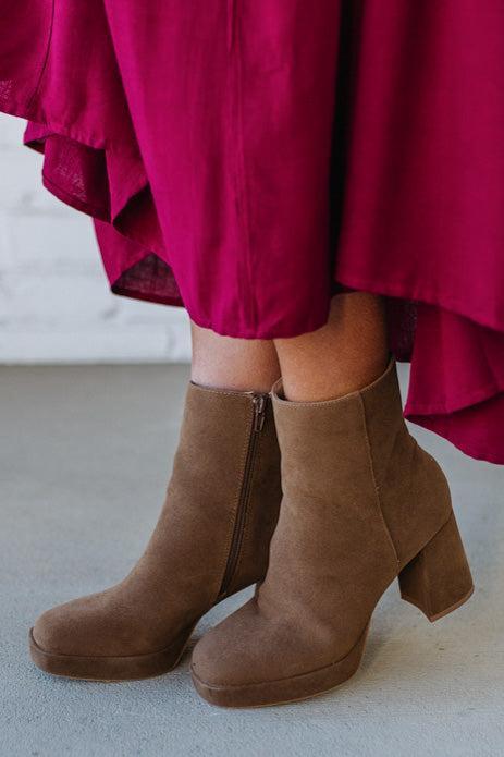 Person wearing brown ankle boots with block heel and smooth faux suede finish.