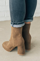 Person wearing brown ankle boots with block heel and smooth faux suede finish.