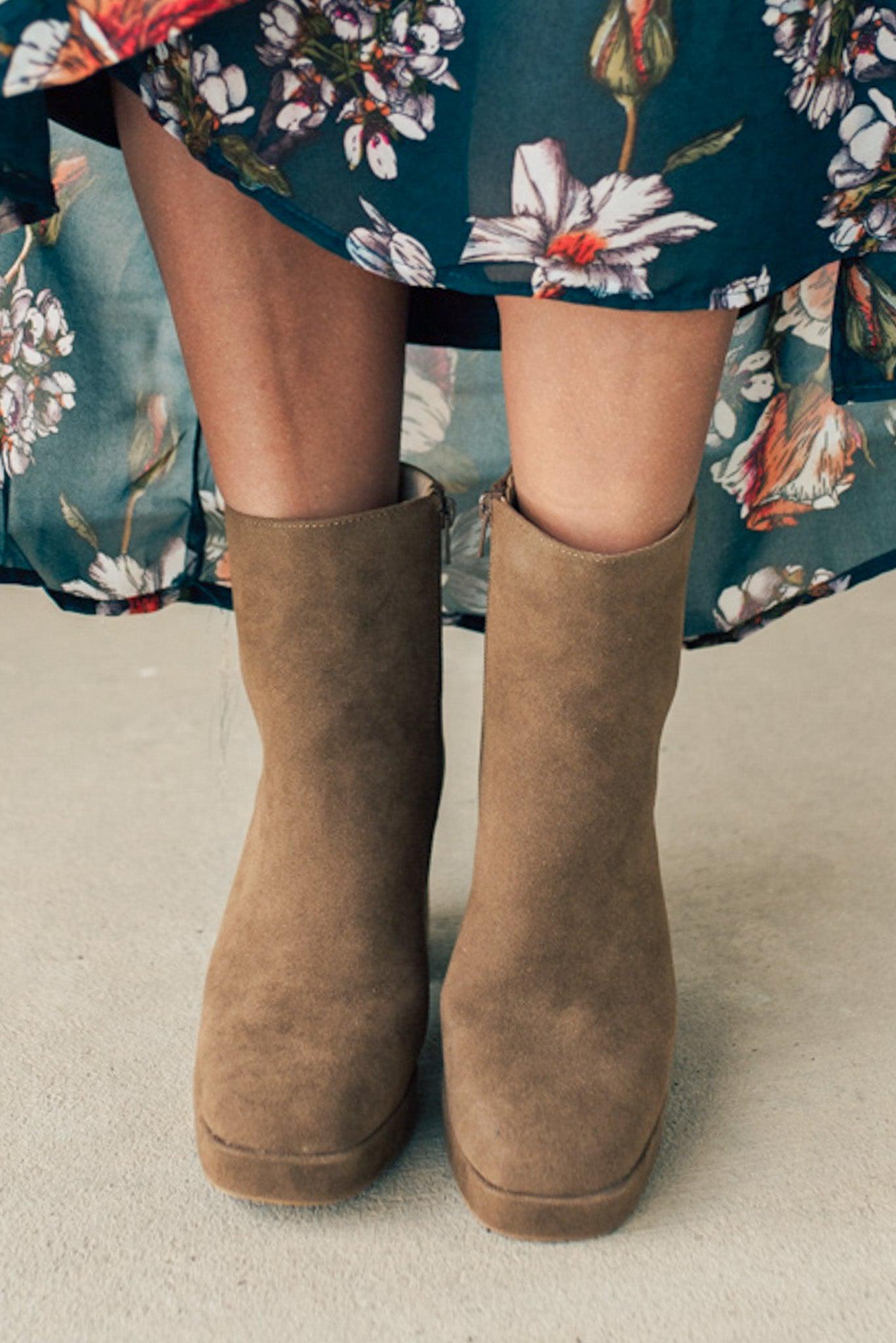 Person wearing brown ankle boots with block heel and smooth faux suede finish.
