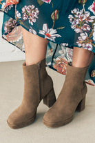Person wearing brown ankle boots with block heel and smooth faux suede finish.