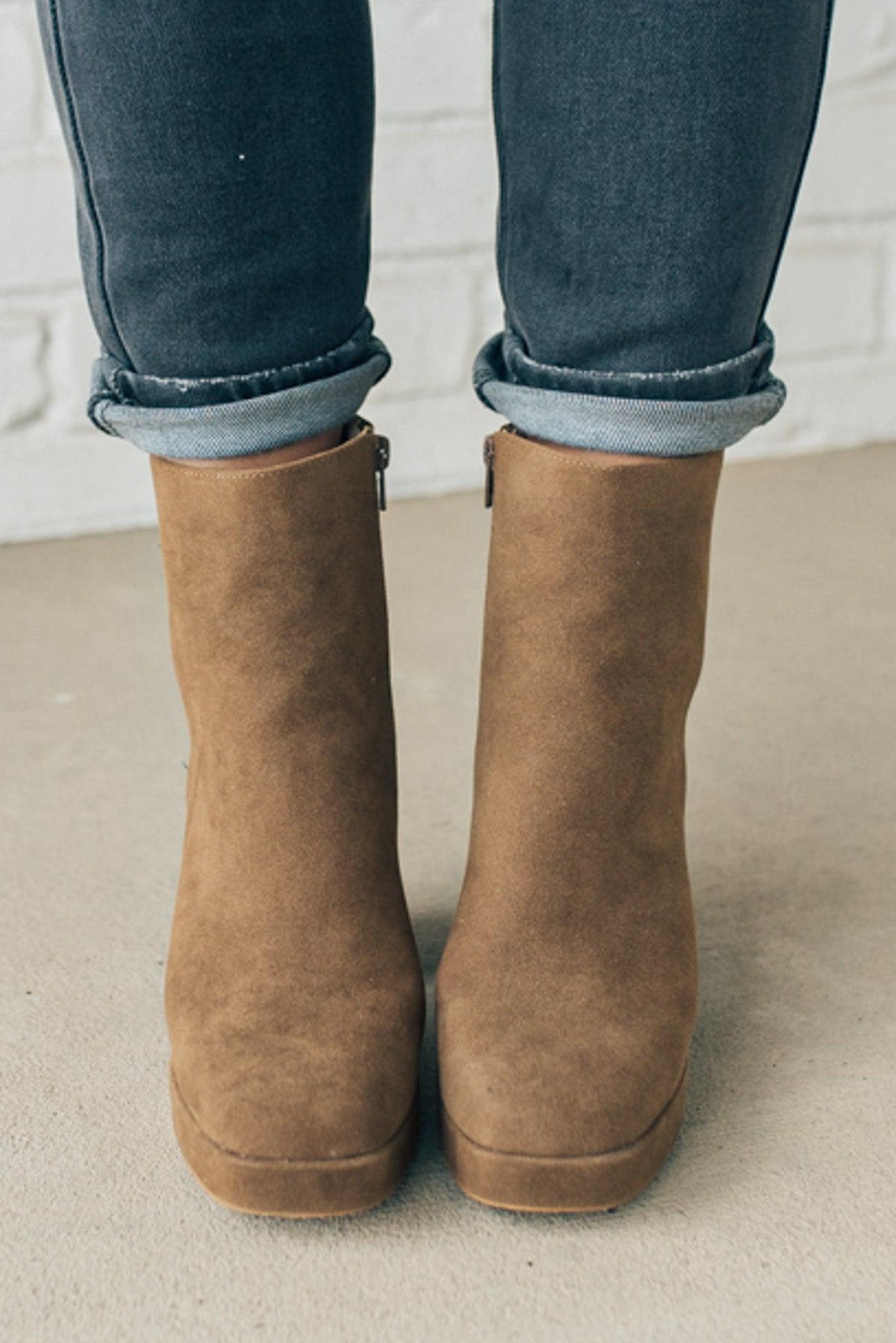 Person wearing brown ankle boots with block heel and smooth faux suede finish.