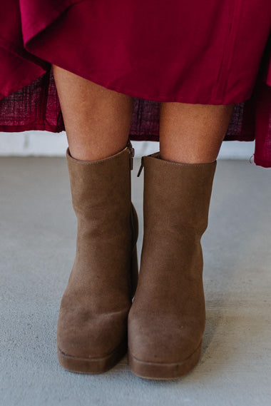 Person wearing brown ankle boots with block heel and smooth faux suede finish.