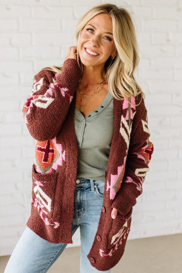 Woman wearing a brown patterned cardigan with a white brick wall background