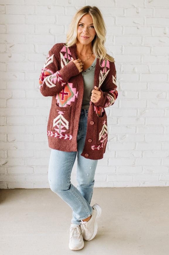 Woman wearing a patterned cardigan in front of a white brick wall