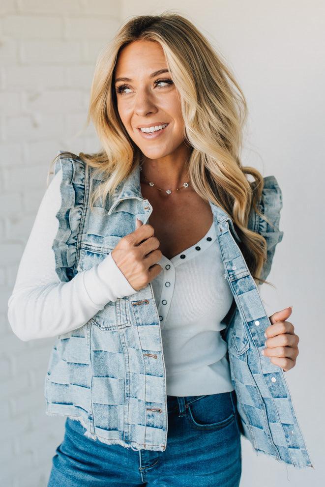 Woman wearing a denim checkered vest over a white shirt against a plain background