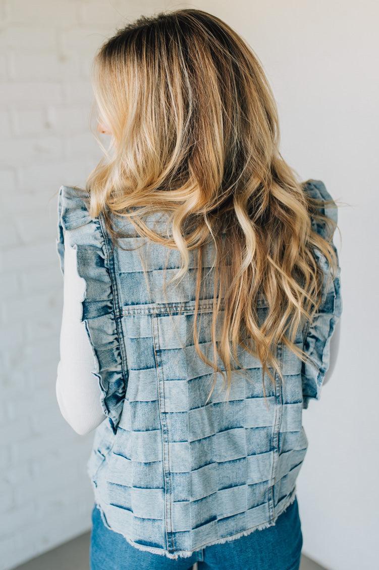 Woman wearing a denim checkered vest over a white shirt against a plain background