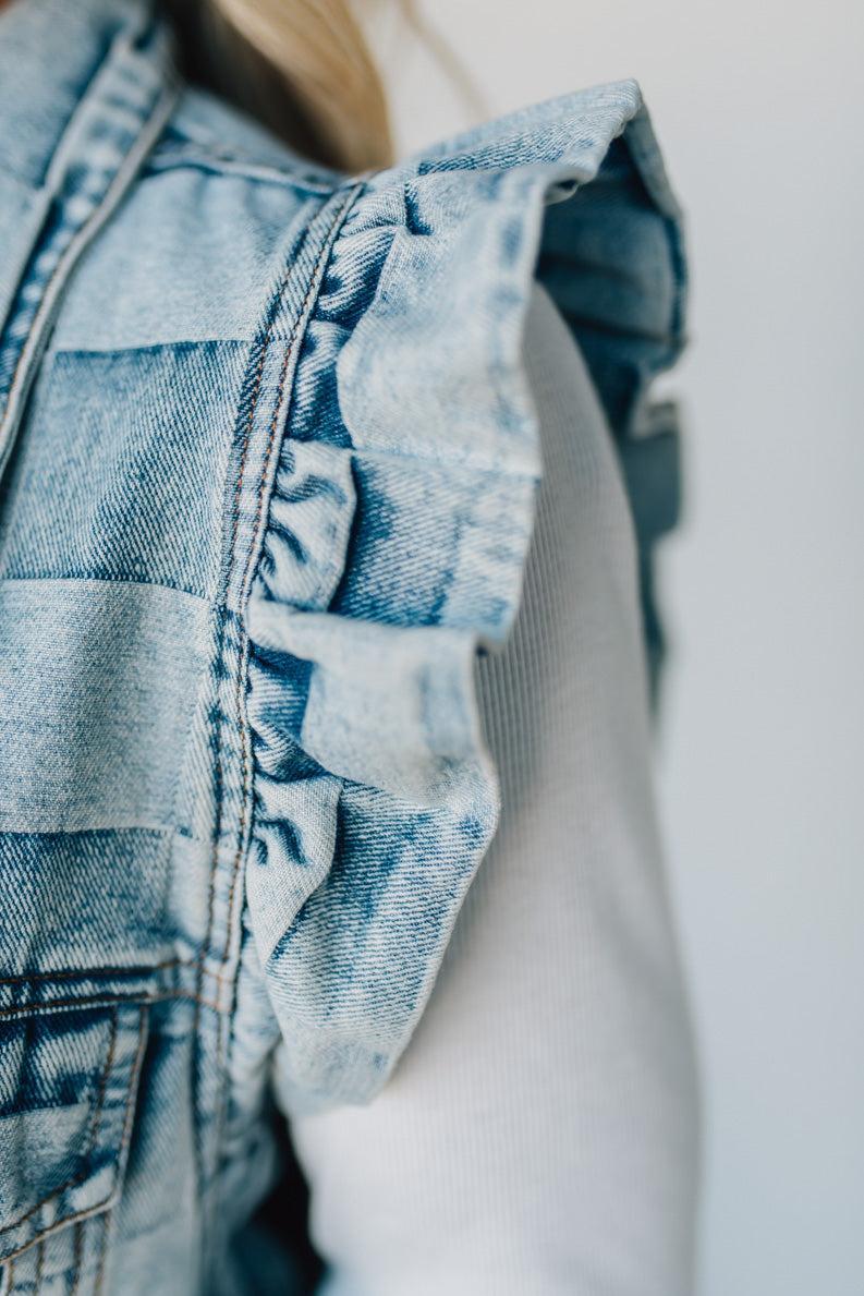 Woman wearing a denim checkered vest over a white shirt against a plain background