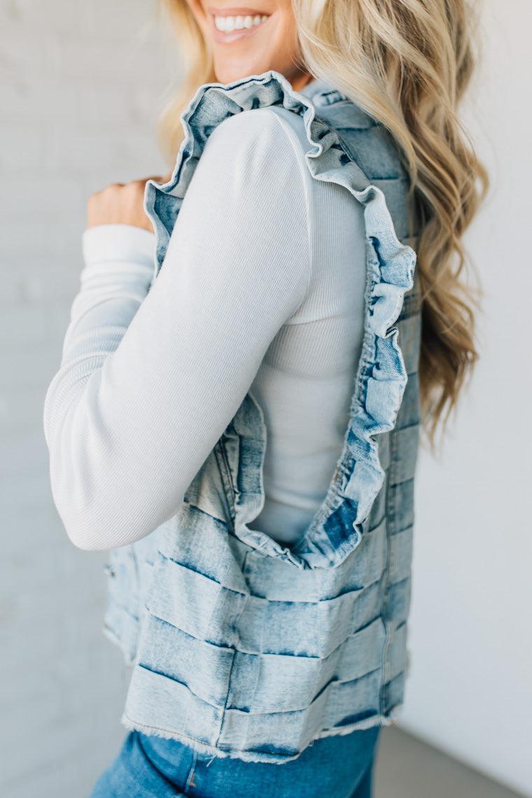 Woman wearing a denim checkered vest over a white shirt against a plain background
