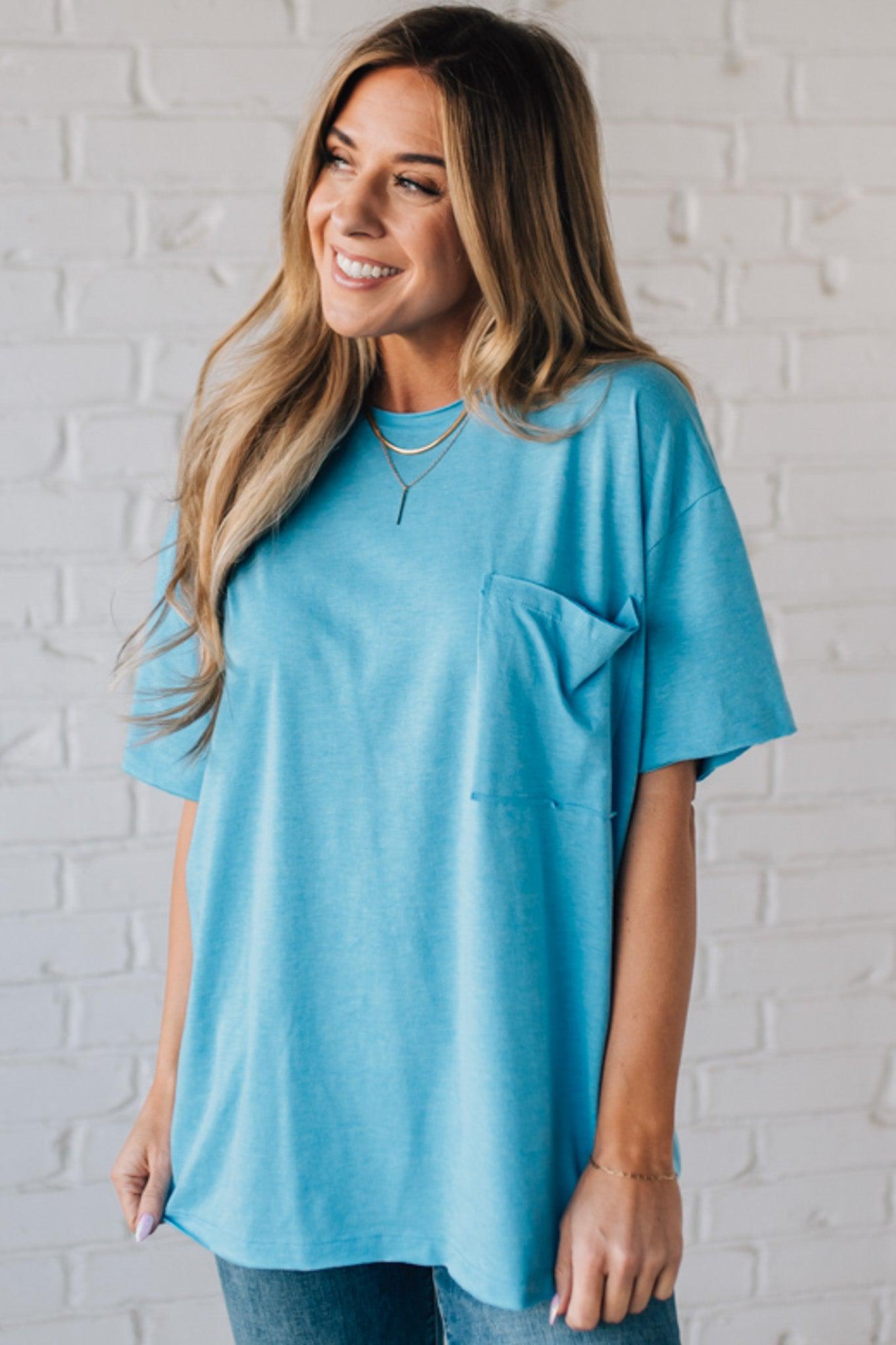 Blonde woman wearing an oversized solid tee with front pocket, and raw scissor cut edges.
