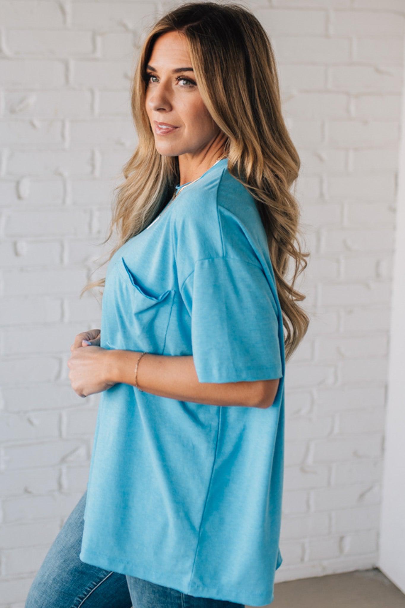 Blonde woman wearing an oversized solid tee with front pocket, and raw scissor cut edges.