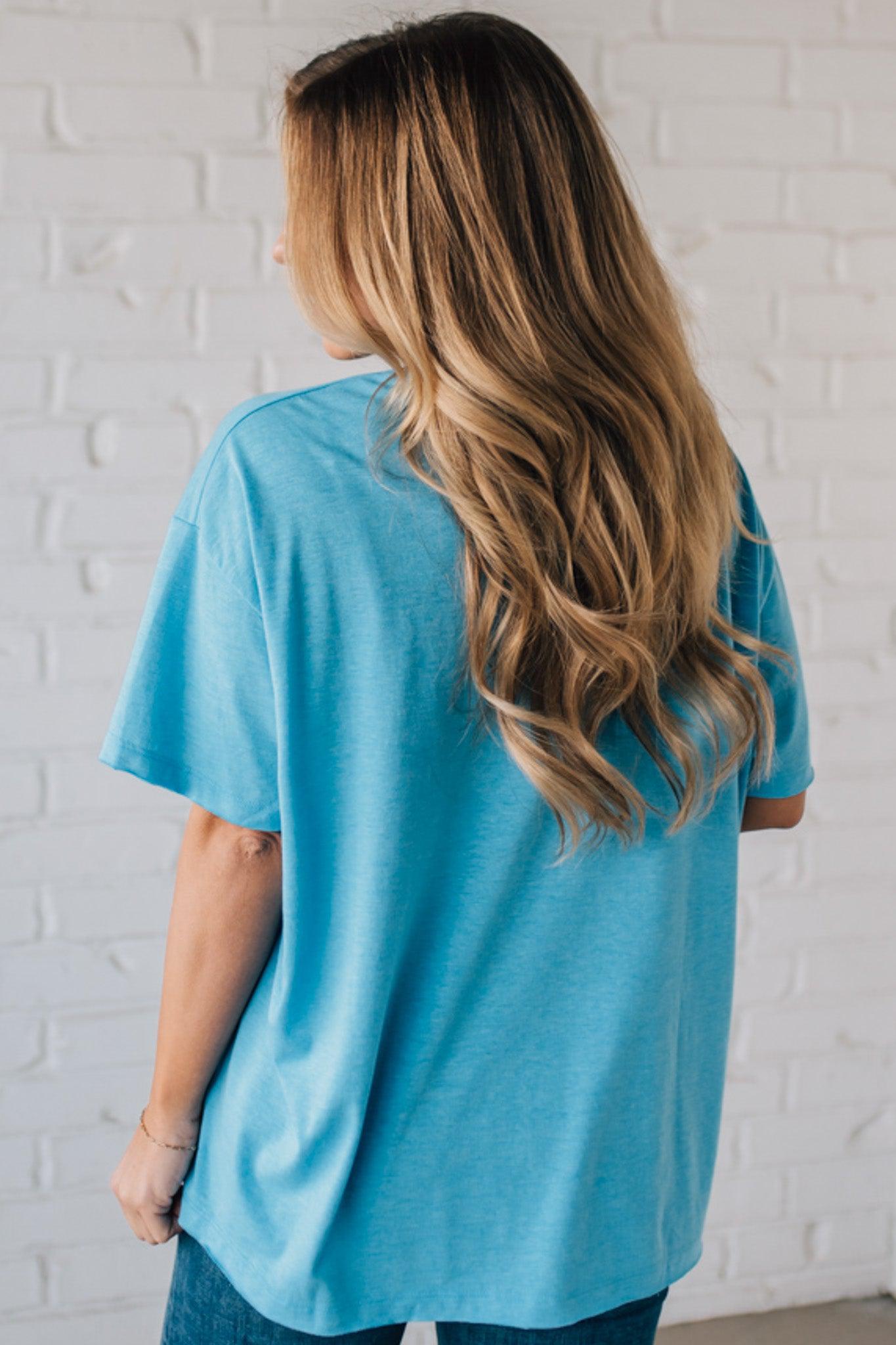 Blonde woman wearing an oversized solid tee with front pocket, and raw scissor cut edges.