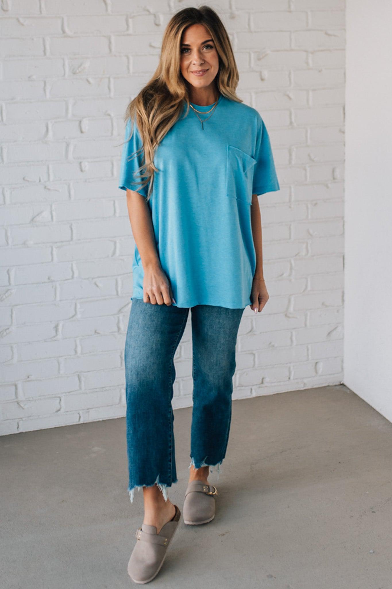 Blonde woman wearing an oversized solid tee with front pocket, and raw scissor cut edges.