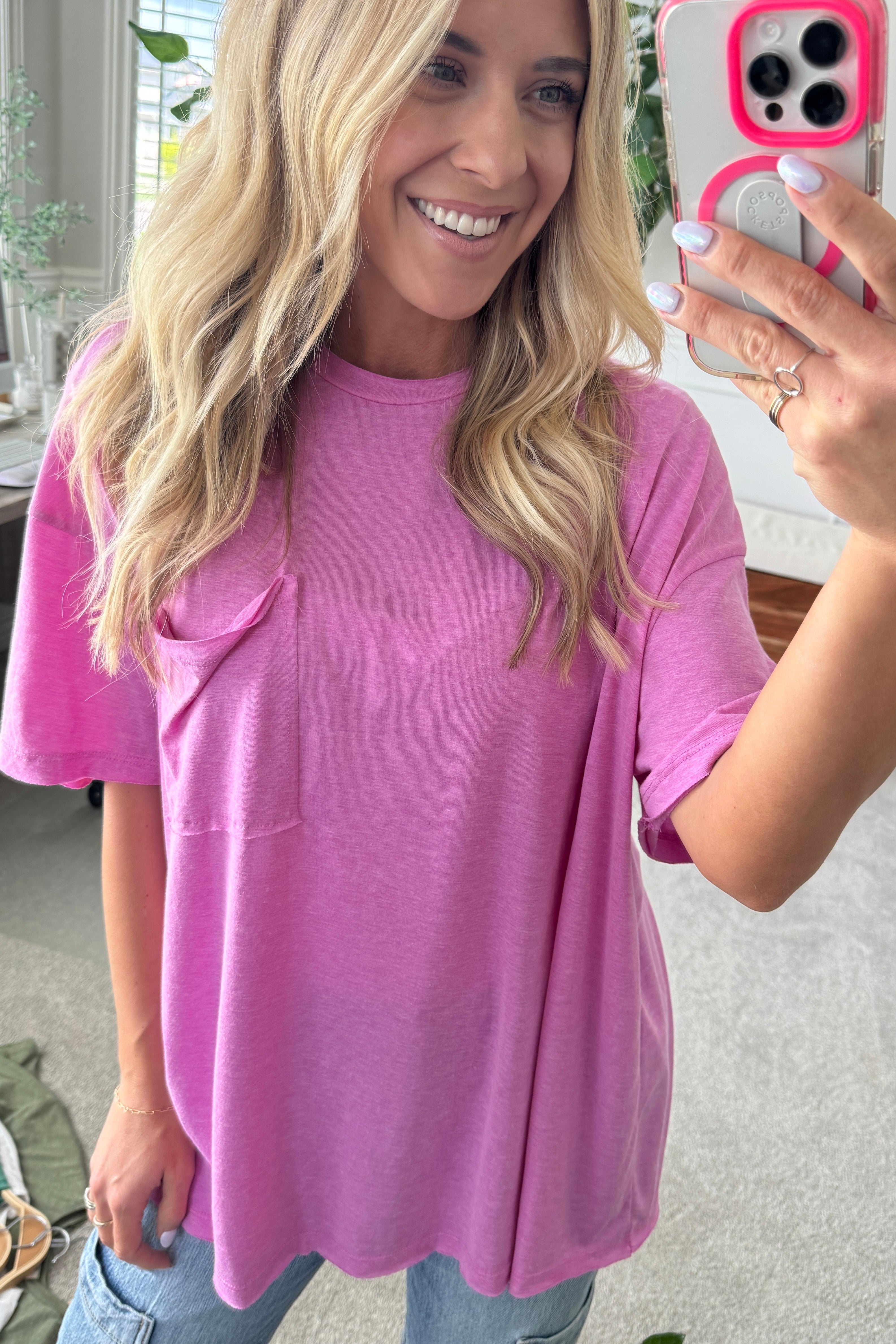 Blonde woman wearing an oversized solid tee with front pocket, and raw scissor cut edges.