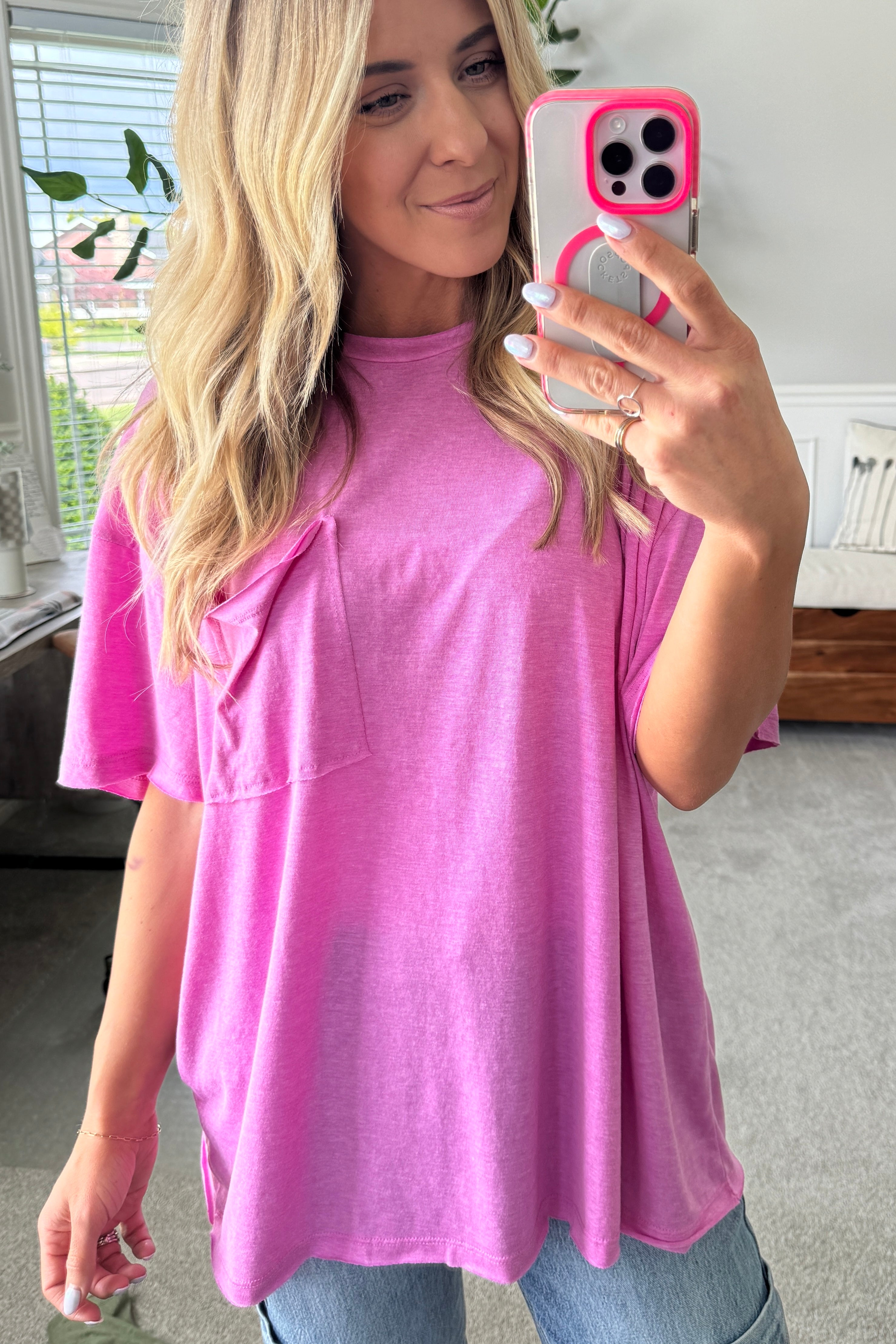 Blonde woman wearing an oversized solid tee with front pocket, and raw scissor cut edges.