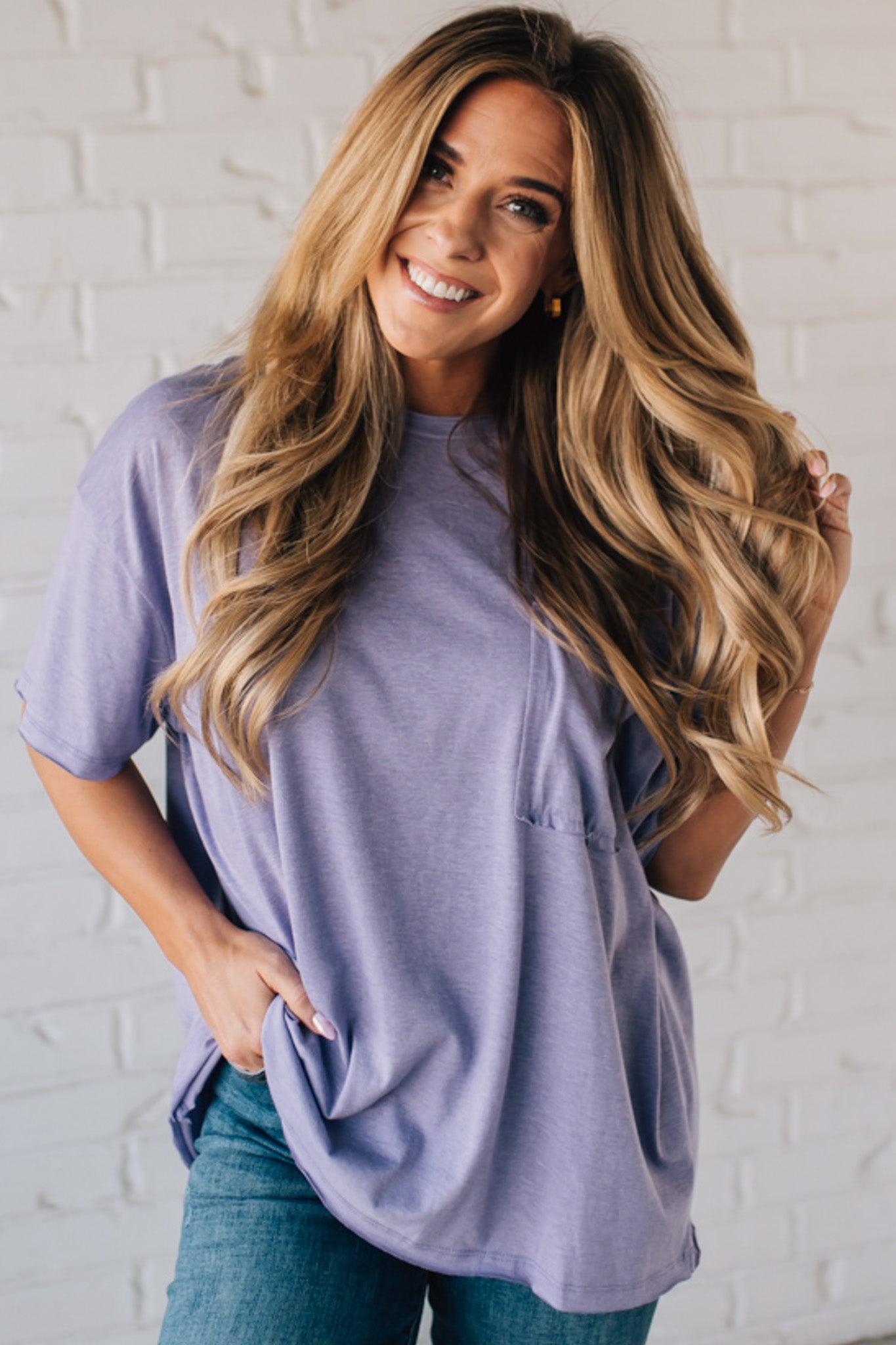 Blonde woman wearing an oversized solid tee with front pocket, and raw scissor cut edges.