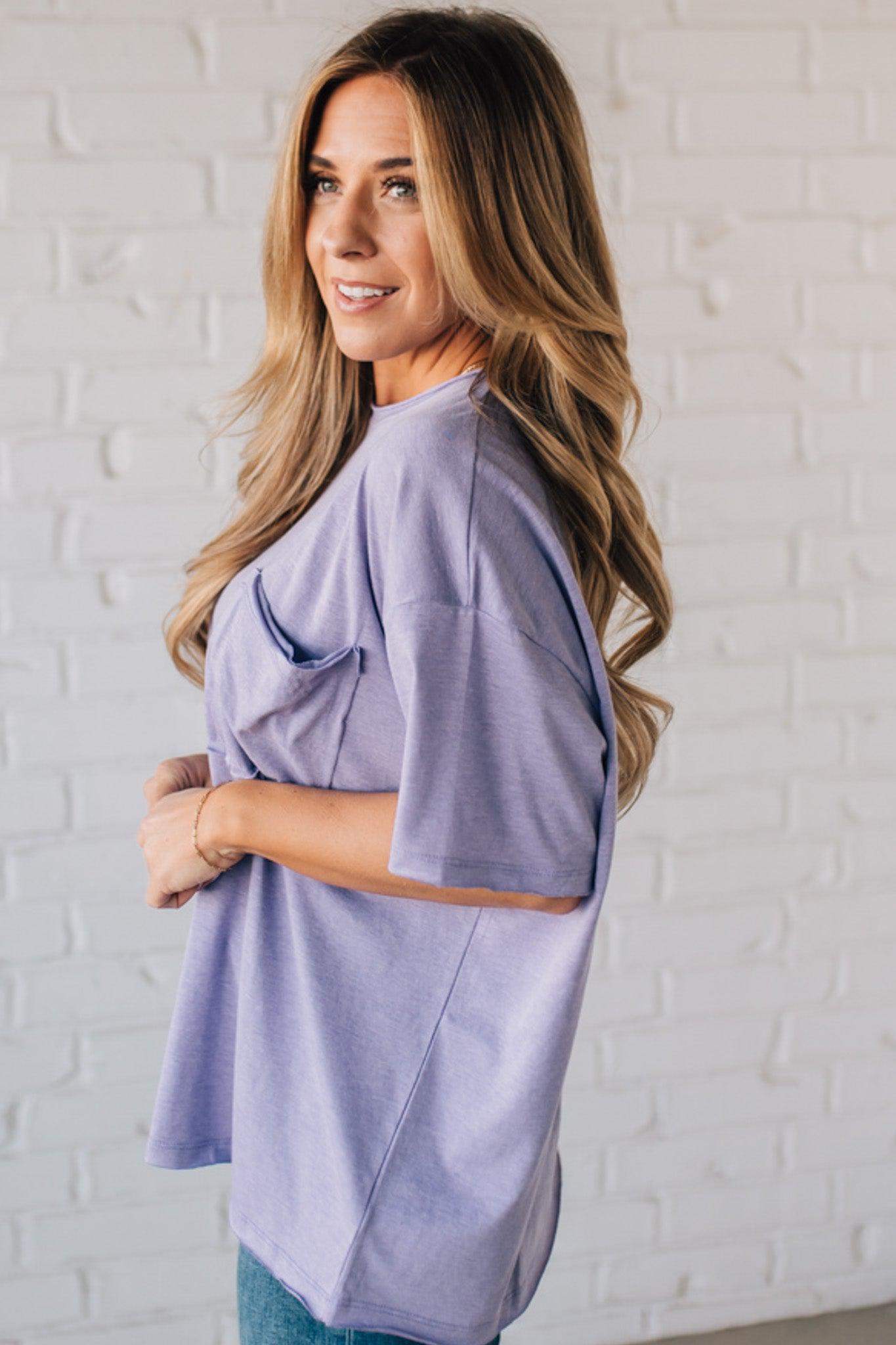 Blonde woman wearing an oversized solid tee with front pocket, and raw scissor cut edges.