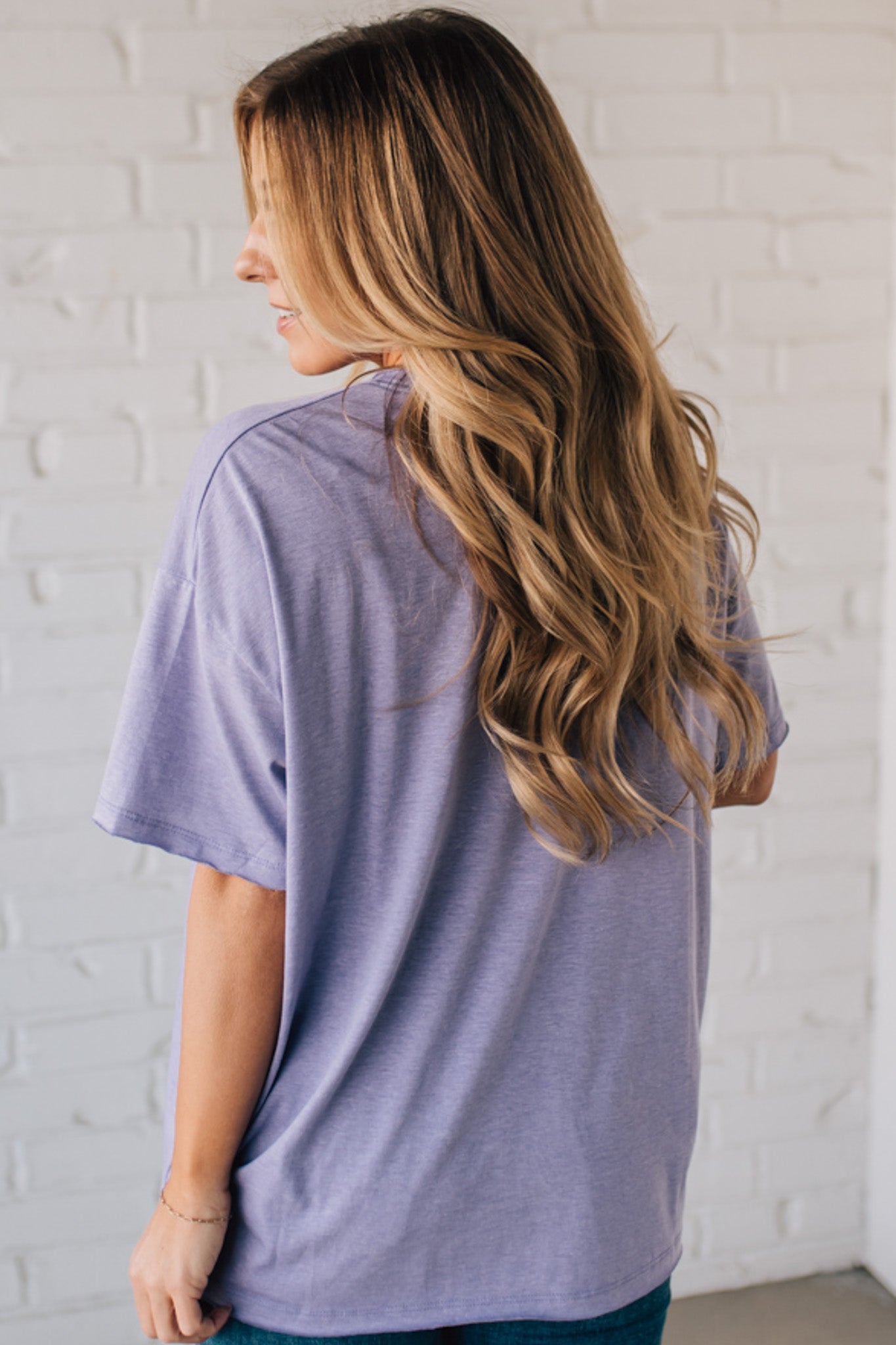 Blonde woman wearing an oversized solid tee with front pocket, and raw scissor cut edges.