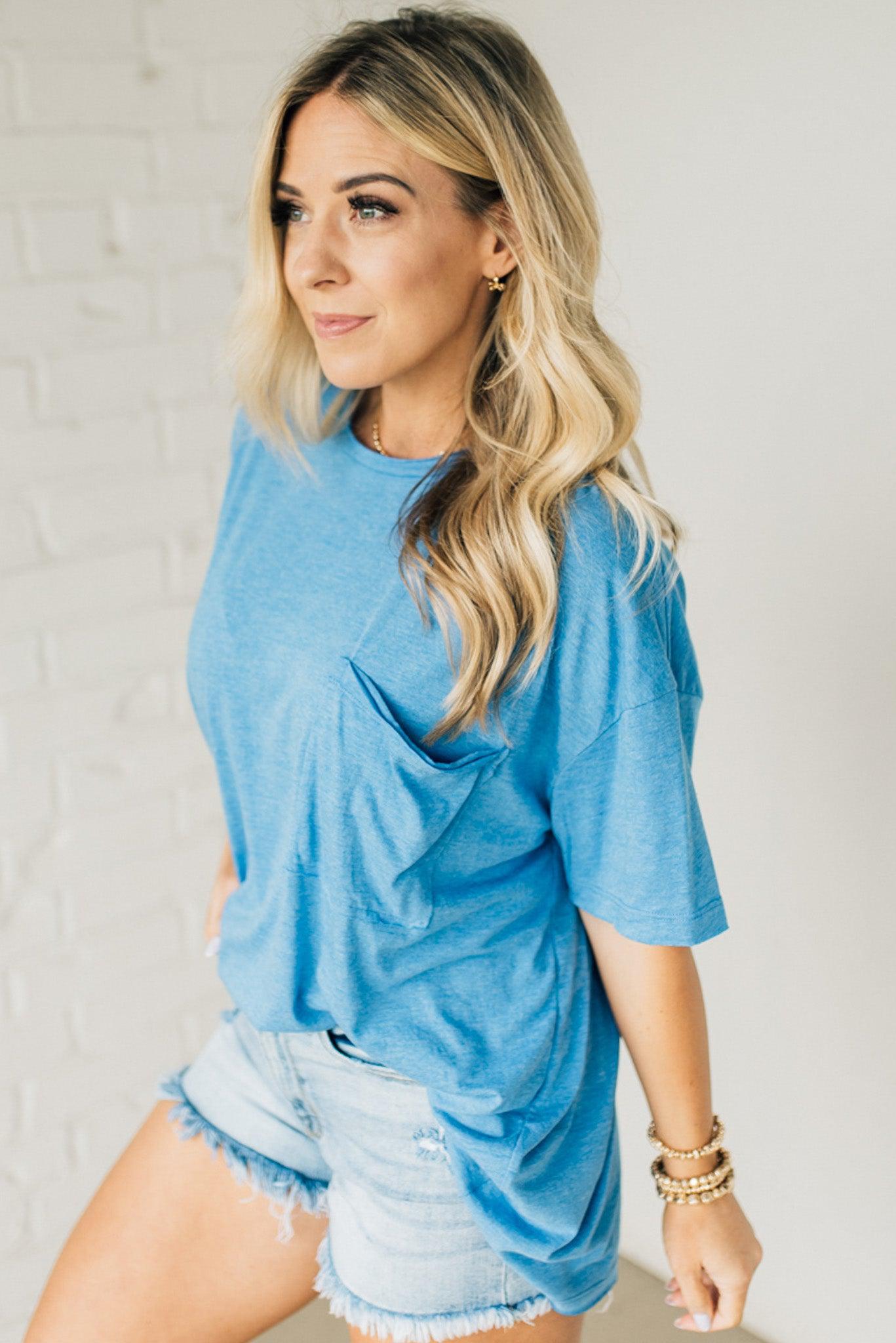 Blonde woman wearing an oversized solid tee with front pocket, and raw scissor cut edges.
