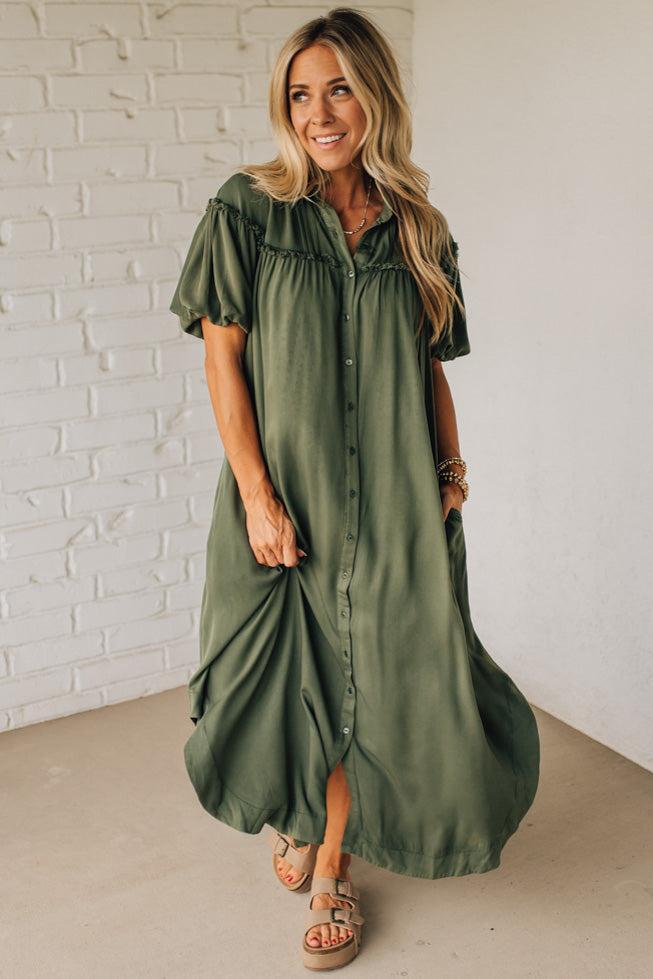 Woman wearing a green dress against a white brick wall.