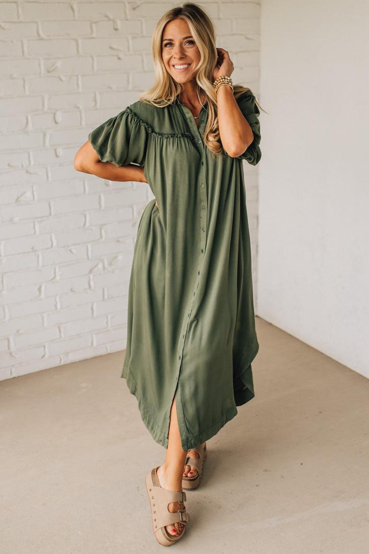 Woman wearing an olive green dress with a white brick wall background
