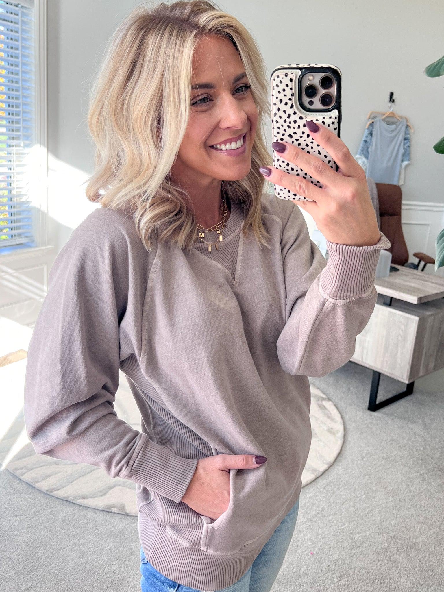 A woman wearing a beige ribbed accent pocketed pullover with dolman sleeves and a round neckline.