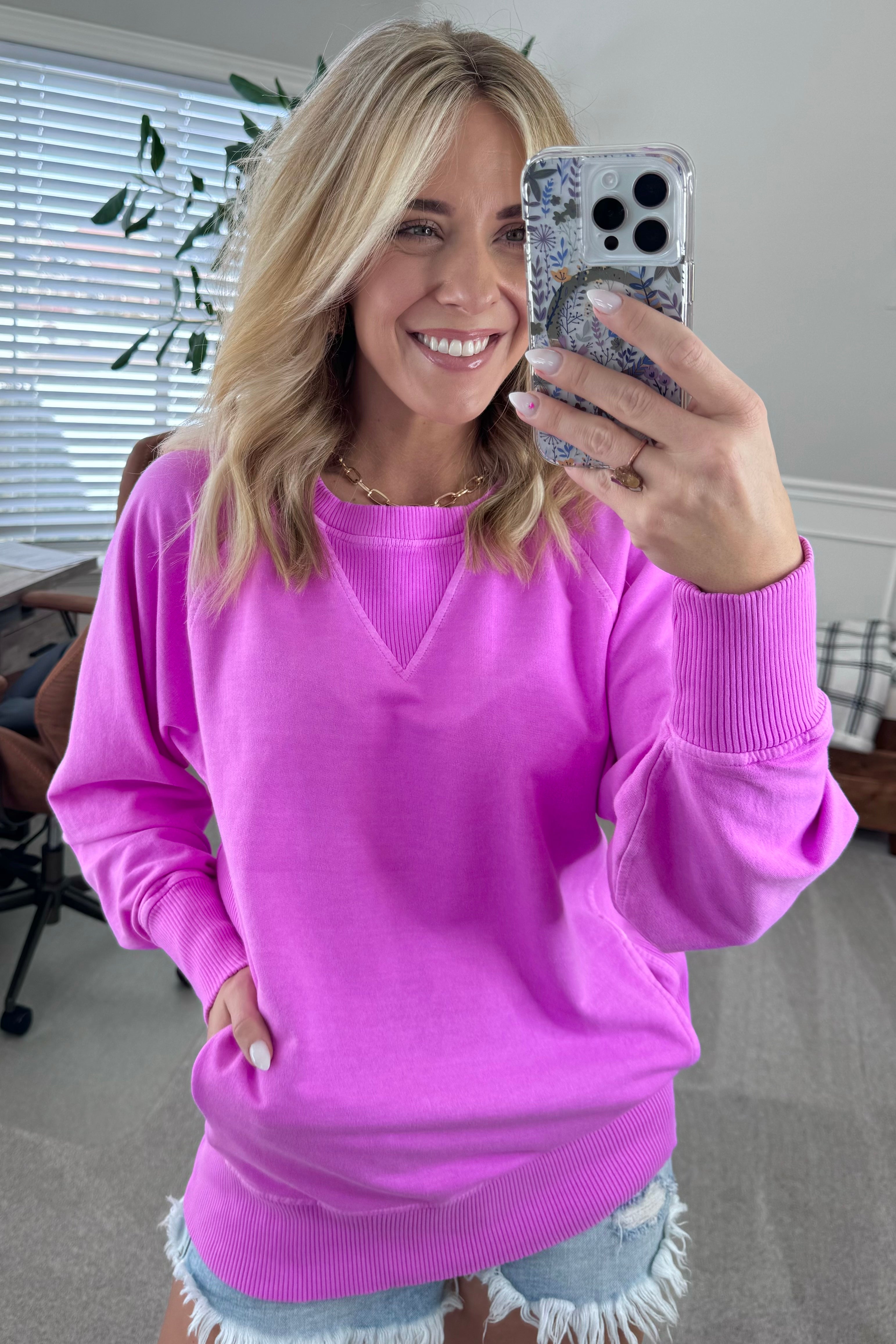 A woman wearing a bright plum ribbed accent pocketed pullover with dolman sleeves and a round neckline.