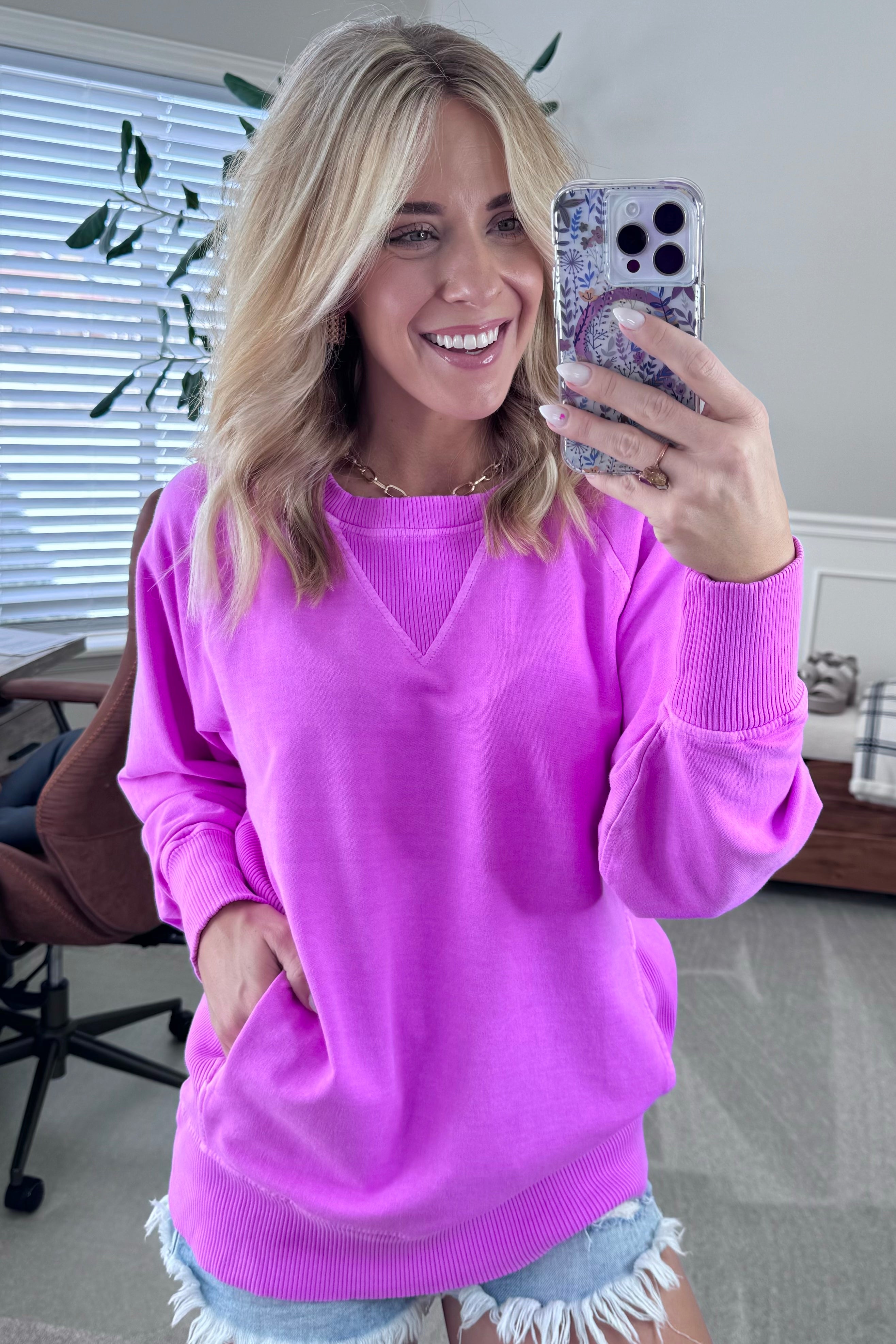 A woman wearing a bright plum ribbed accent pocketed pullover with dolman sleeves and a round neckline.