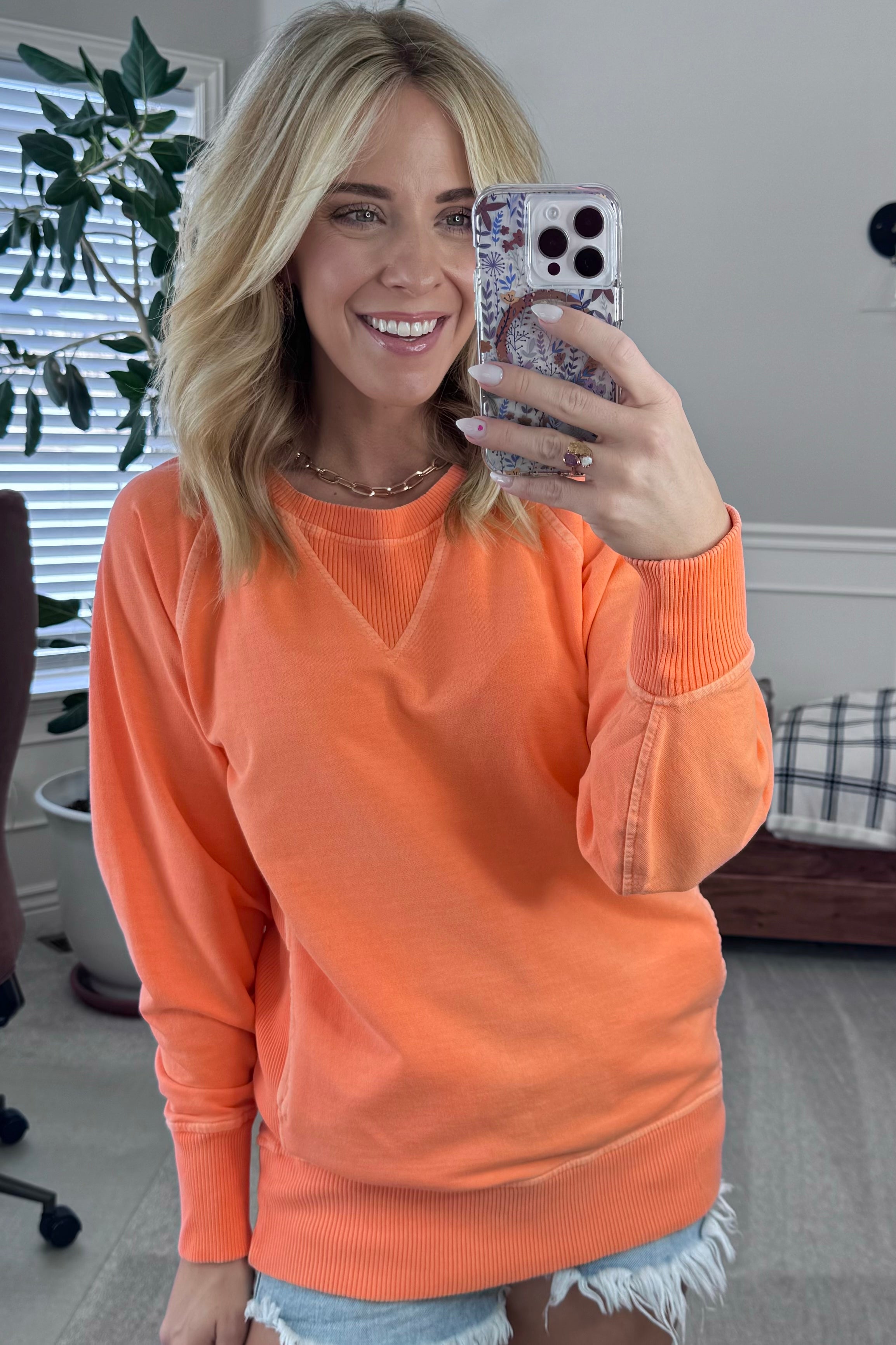 A woman wearing an orange ribbed accent pocketed pullover with dolman sleeves and a round neckline.