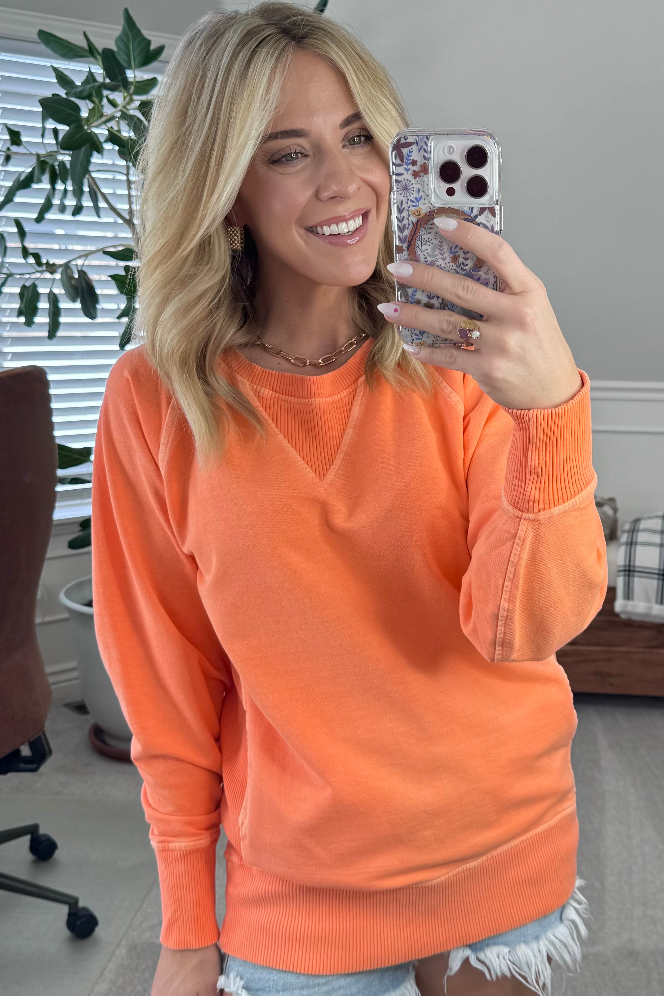 A woman wearing an orange ribbed accent pocketed pullover with dolman sleeves and a round neckline.