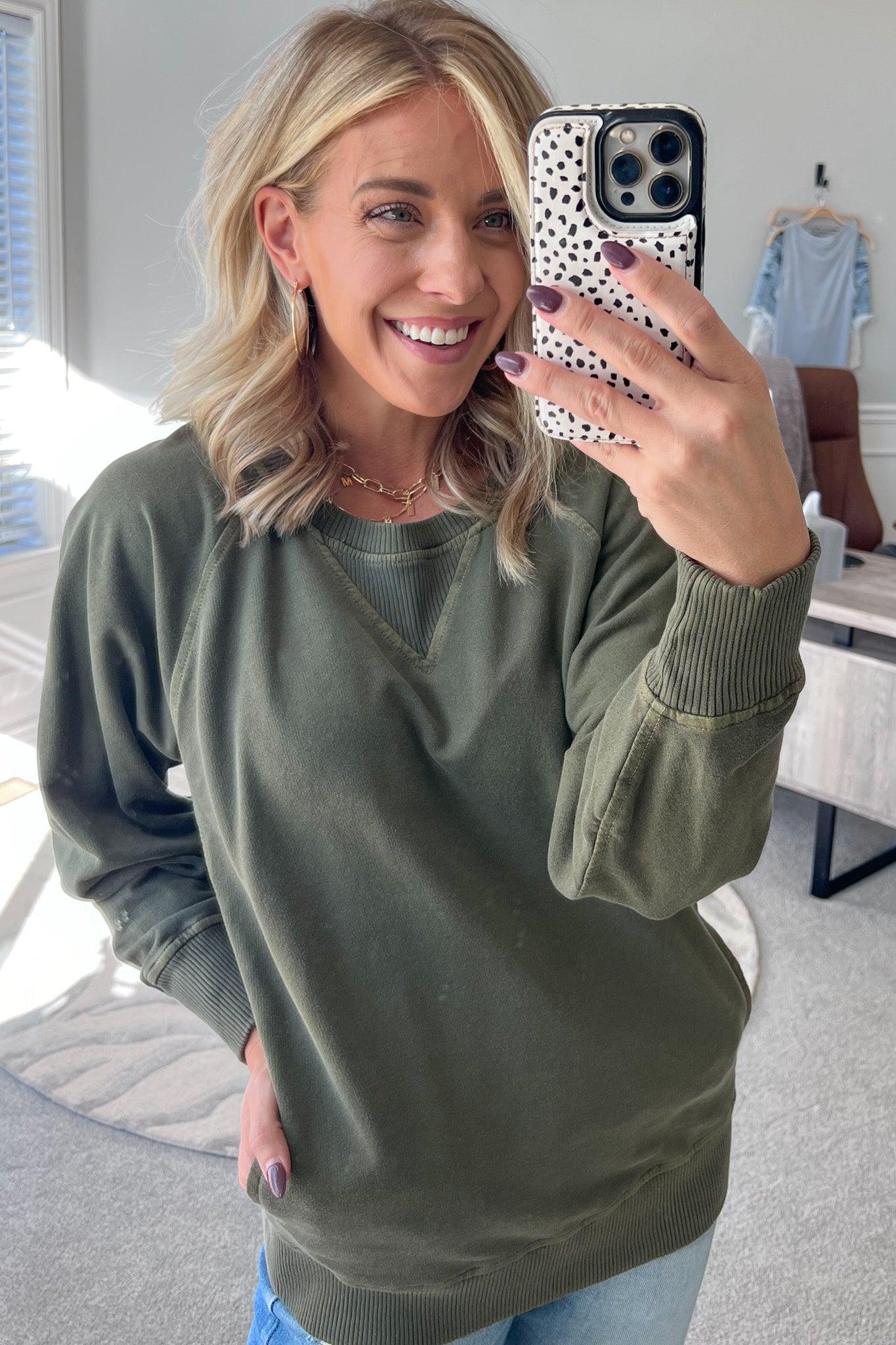 A woman wearing a olve ribbed accent pocketed pullover with dolman sleeves and a round neckline.