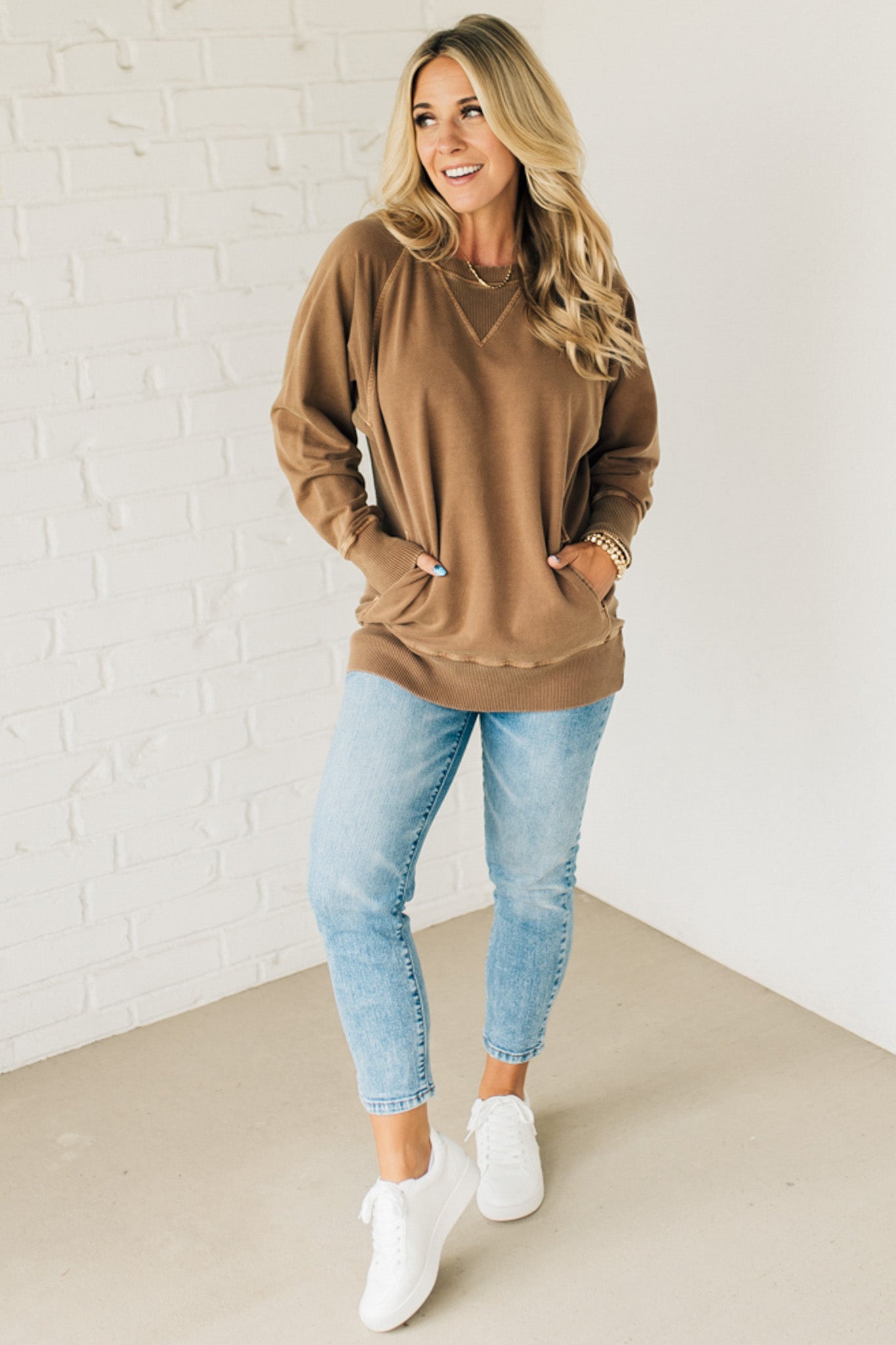 A woman wearing a brown ribbed accent pocketed pullover with dolman sleeves and a round neckline.